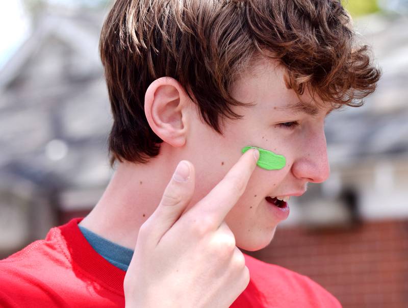 Newton students on May 4 paint their faces before painting Christmas light displays for the city's Maytag Park Holiday Lights during Red Pride Service Day.