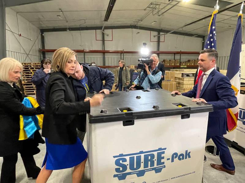 Iowa Gov. Kim Reynolds and Sen. Zach Nunn fasten the lid to a box containing safety equipment during a March 30 press conference in which the state announced it would be sending helmets and ballistic vests to Ukraine.