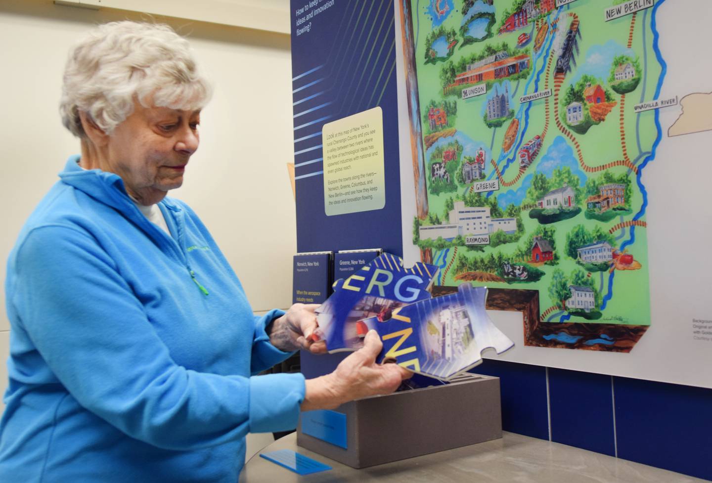 Judie O’Connor, a volunteer for Jasper County RSVP, shows off an interactive display at the Spark: Places of Innovation traveling exhibit that requires guests to put together a puzzle.