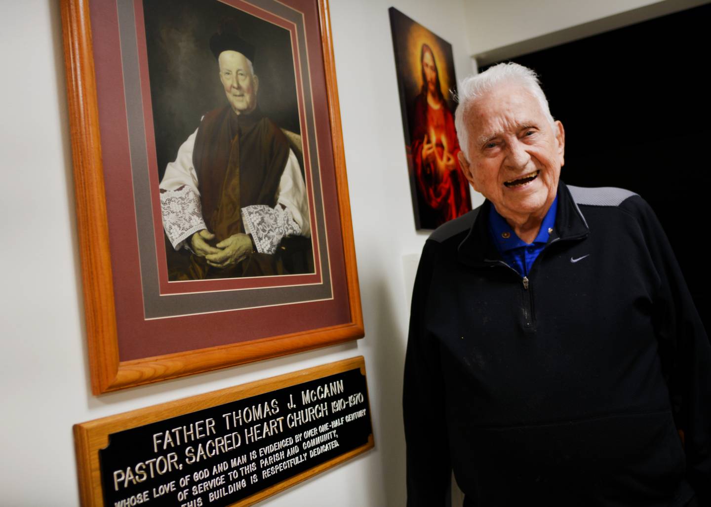 John McNeer, a member of the Knights of Columbus, stands next to a portrait of Monsignor Thomas McCann, who was pivotal in starting a tradition of bell ringing for the Salvation Army in Newton.