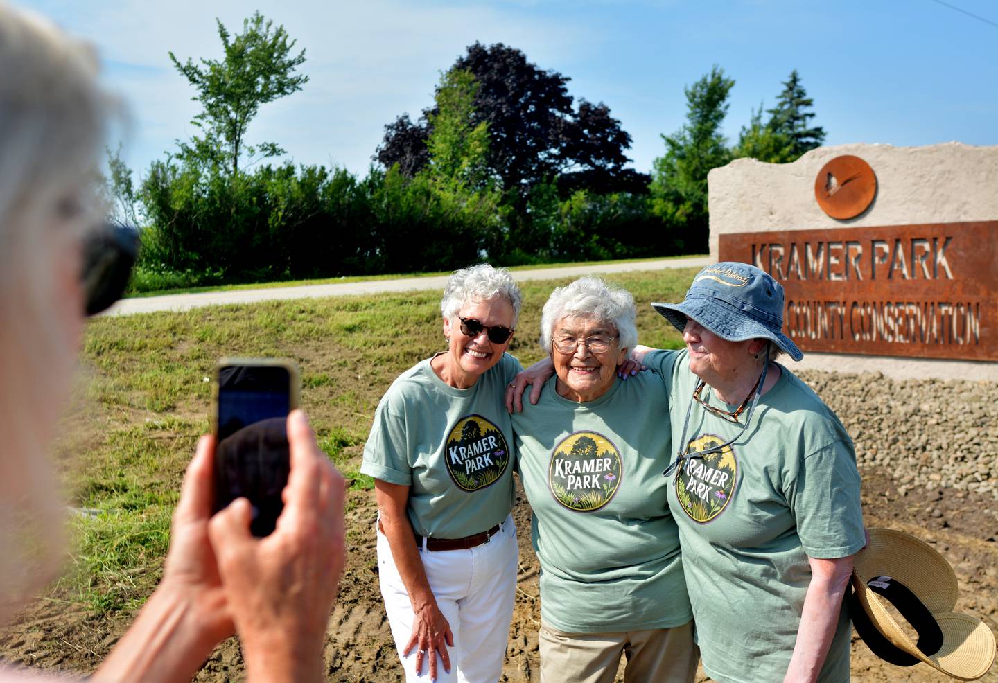 From left: Katy Kramer Lee, Carol Kramer and Anne Yakle pose for a photo next to the Kramer Park sign. Kramer Park is where the nature center is currently being constructed.