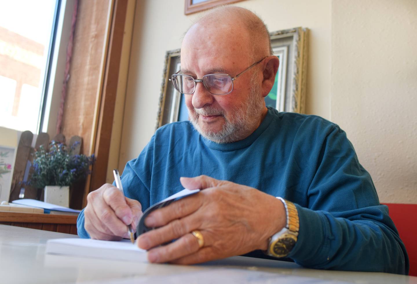 Phil Muta signs a copy of his first book, "Camp Laura," during a book signing March 27 at PJ's Deli in Newton. "Camp Laura" is based on the real experiences Muta had as a teenager working at a camp in Pennsylvania. The 80-year-old wanted to tell this story for several decades but did not find the time until recently.