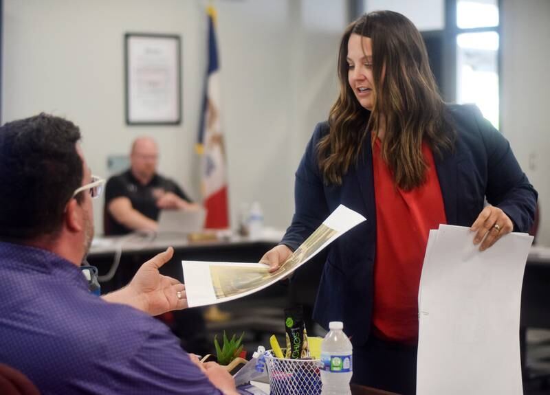 Rachelle Hines, a partner with FRK Architects + Engineers, hands school board member Travis Padget a copy of a presentation she gave May 9 about the options for Newton's home baseball field, which is currently owned by the city and received heavy damage from a March storm.