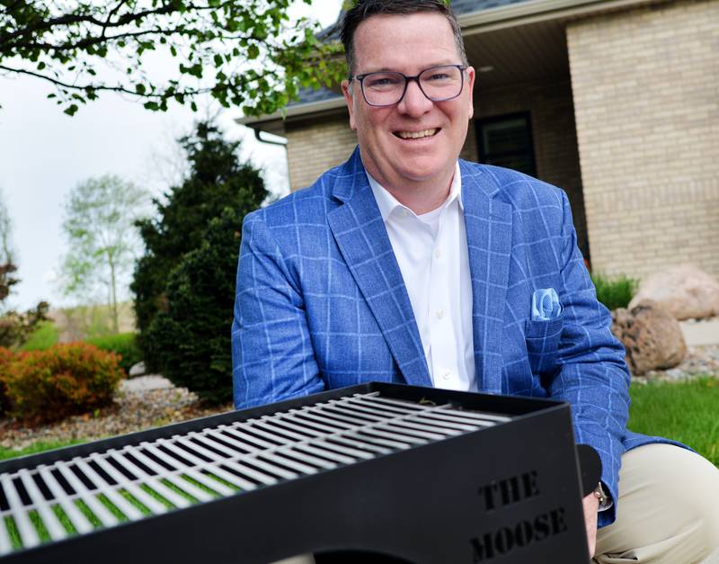 Mark Allen, of Newton, stands next to The Moose Fireplace Grill, a product he developed that has found a new way to enjoy grilling, tailgating and camping. Manufactured by Red Oak Fabrication, the product allows for woodfire grilling and cooking and recreates the experience of friends and family hanging out in front of a fireplace.
