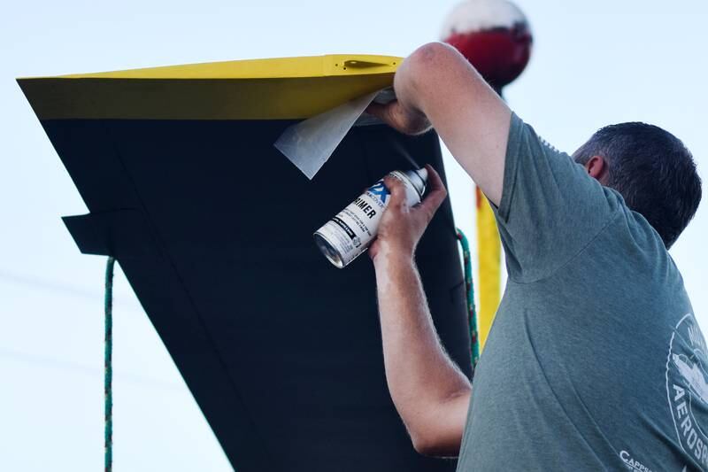 Joe Giannini of Midwest Aerospace applies spray paint and other finishing touches to the Huey helicopter's rotor blade before placing it on its post near other memorials to veterans in downtown Baxter.